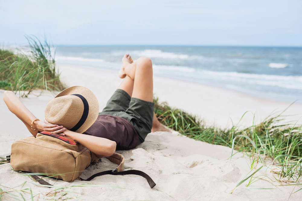 Young woman resting by the sea. Girl lying down on the beach. Enjoying life, summer lifestyle, relaxation, mindfulness and travel concept